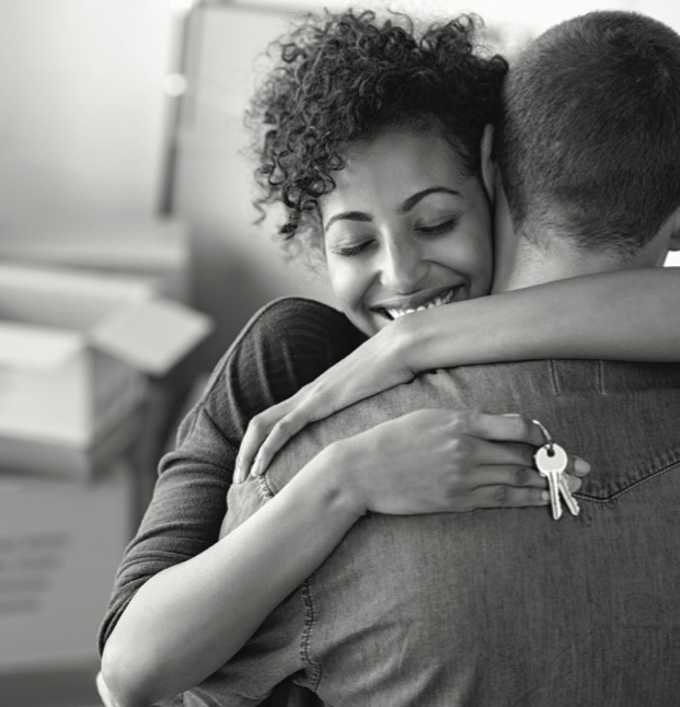 A woman hugs a man with a pair of keys in her hand and a smile on her face.