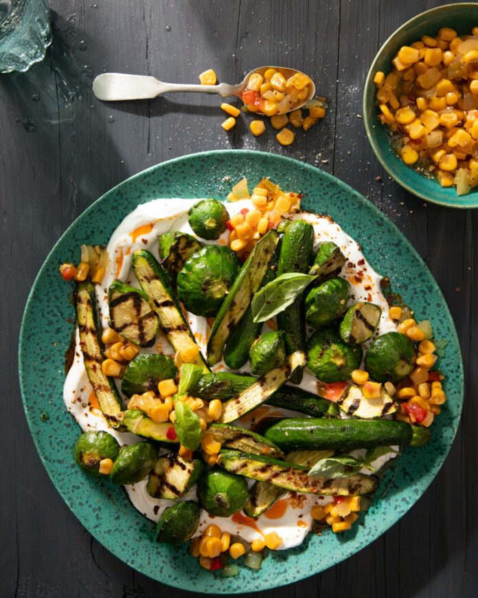a plate of grilled zucchini in a yogurt sauce adn with a corn relish sits on a green plate witha. fork full above it.