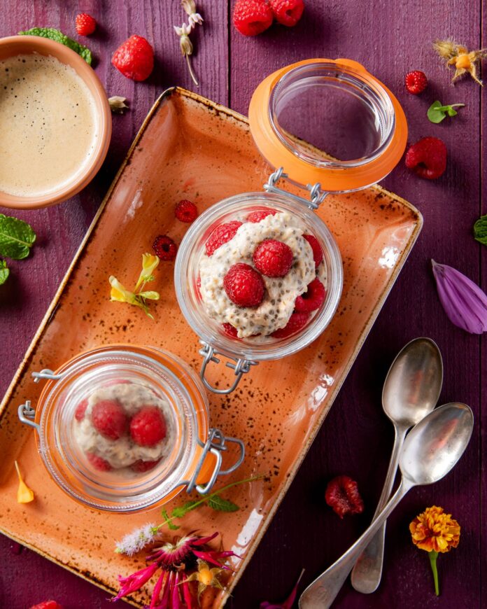 clear glass jars with overnight chia oats and raspberries set in an orange dish on a purple table