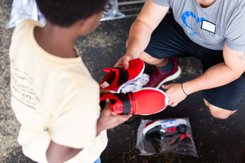 The hands of a man handing a young boy a pair of red tennis shoes.