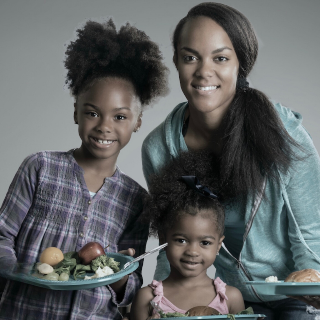 A woman and two children holding plates of food while looking at the camera and smiling.