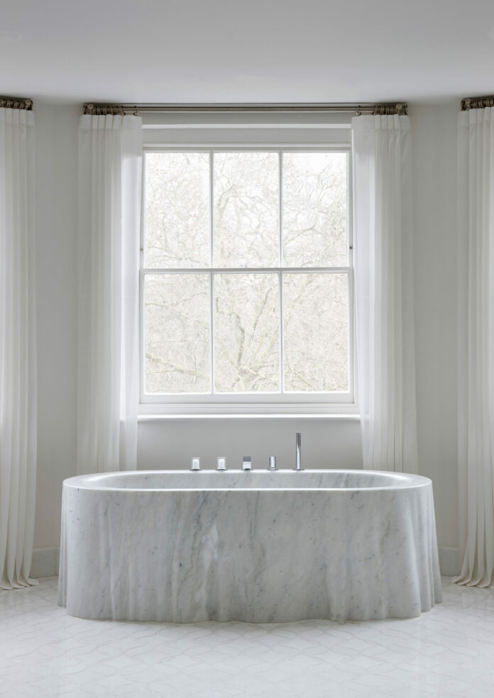 Ancient and Modern A photo of a marble bath tub in a pale gray room in front of a large window.