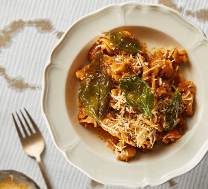 Carrot Bolognese, rich in orange and green color, sits in a white bowl. Off to the left is a rose gold fork.