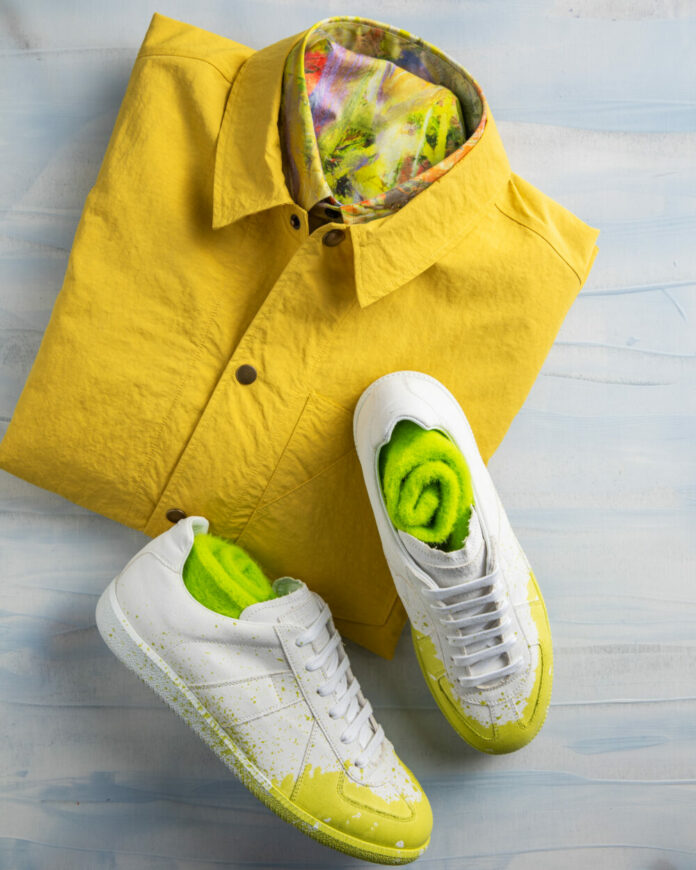 A photo of a folded yellow shirt and white sneakers with green socks tucked inside.