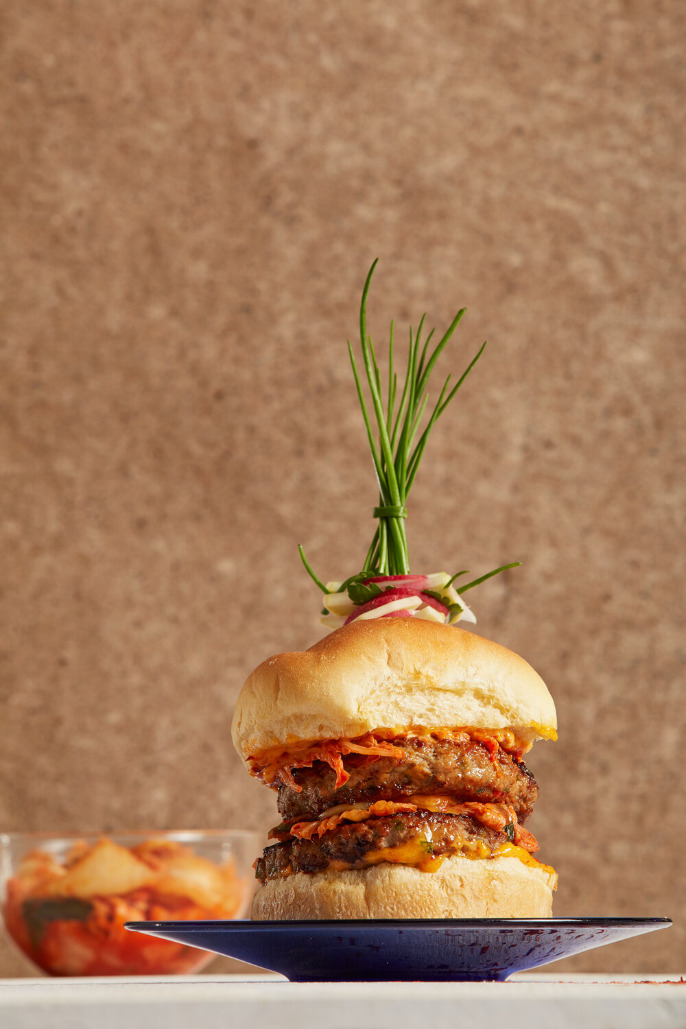 a thick double burger made of lamb with a fancy herb garnish on top on a black plate with a brown background