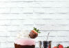 The Milkshake Factory’s Boozy Chocolate-Dipped Strawberry Milkshake Chocolate-Dipped Strawberry Milkshake sits in a milkshake glass, pink in color. A strip of chocolate goes across the middle of the glass.