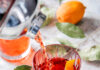 9 Pittsburgh Restaurants Rich in Cocktail Culture Red cocktail being poured into a clear glass from a silver cocktail shaker on a white table with leaves and citrus