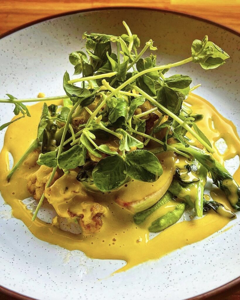 a vegetable dish of carrot Spatzle with a yellow sauce and topped with micro greens