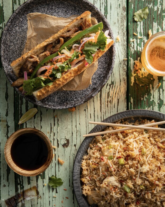 a sandwich on a plate and fried rice in a bowl on a green wood surface