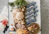 A DIY Kentucky Derby Party along board with meats and cheeses and other snack foods with a fancy hat to the left and blue and white cloth napkins rolled into horseshoe napkin rings on the right