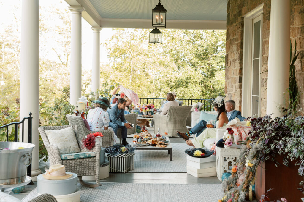 a large porch with wicker furniture and seven people dressed for a Kentucky Derby party
