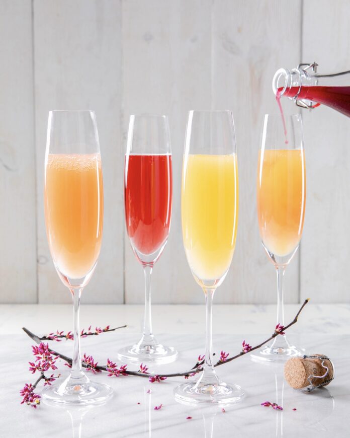 4 champagne glasses with an orange a red a yellow and a peach colored mimosa
