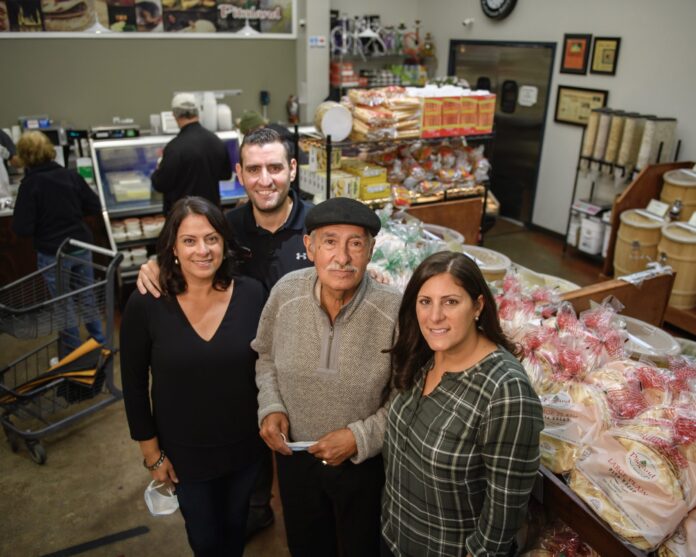 4 people standing in the middle of a small grocery store next to a display of packaged pita bread
