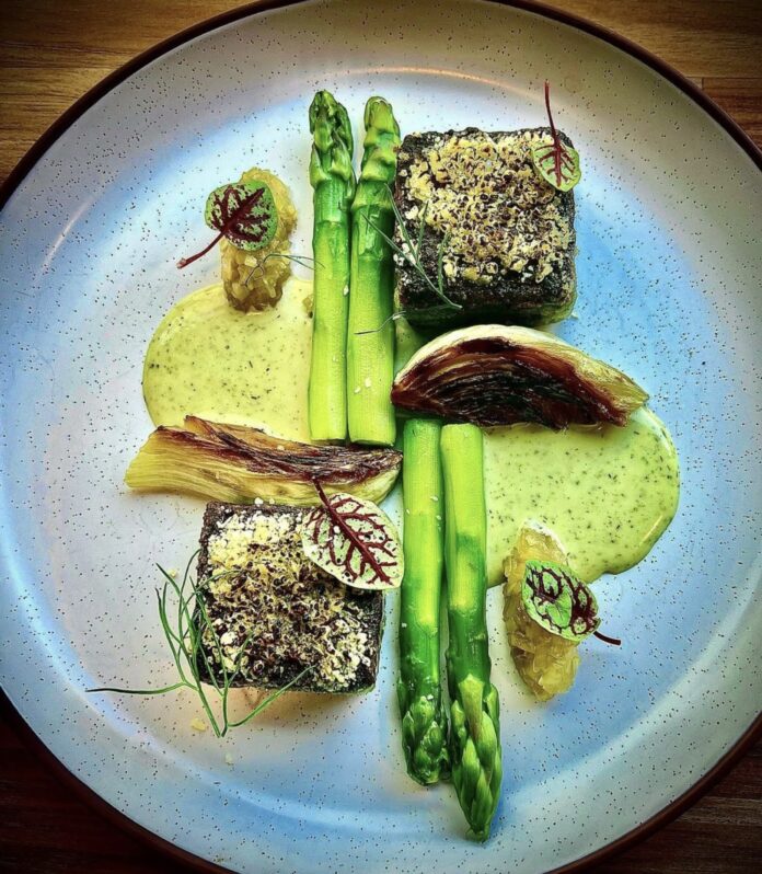 a round plate with asparagus, ramps, salmon roe and spinach with a cream sauce