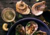Find the Catch of the Day at These 5 Pittsburgh Eateries 7 roasted oyster with corn and herb garnish on a blue plate and 2 oyster shells and a beer sitting on a dark colored surface. seafood dishes