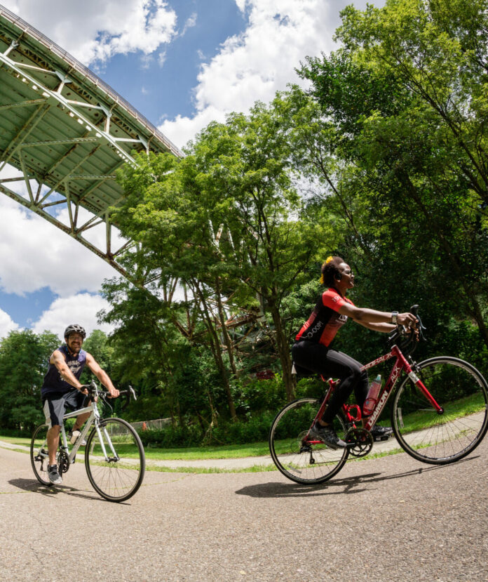 Two bikers bike under a bridge and blue skies in Pittsburgh, Pittsburgh bike trails