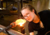 The Pittsburgh Glass Center is Blowing Minds A white woman with french braids and glasses concentrates on blowing glass.