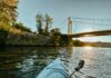 The Best Spots for Boat Lovers to Enjoy the Monongahela River The tip of kayak is shown sitting on the Monongahela River, looking at a yellow bridge