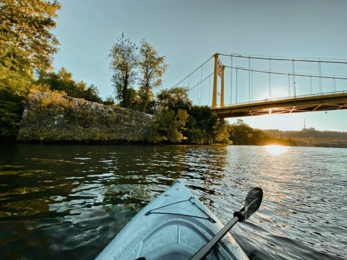The tip of kayak is shown sitting on the Monongahela River, looking at a yellow bridge