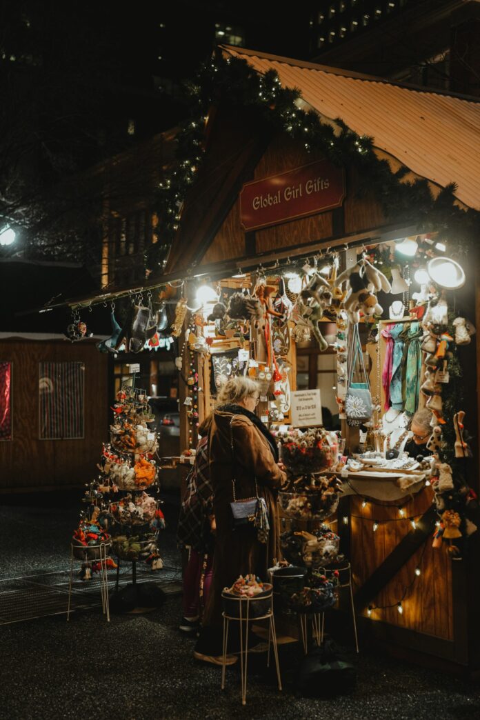 A woman bundled in warm clothes stands at a booth selling holiday gifts. It's lit up and festive looking. Pittsburgh holiday traditions