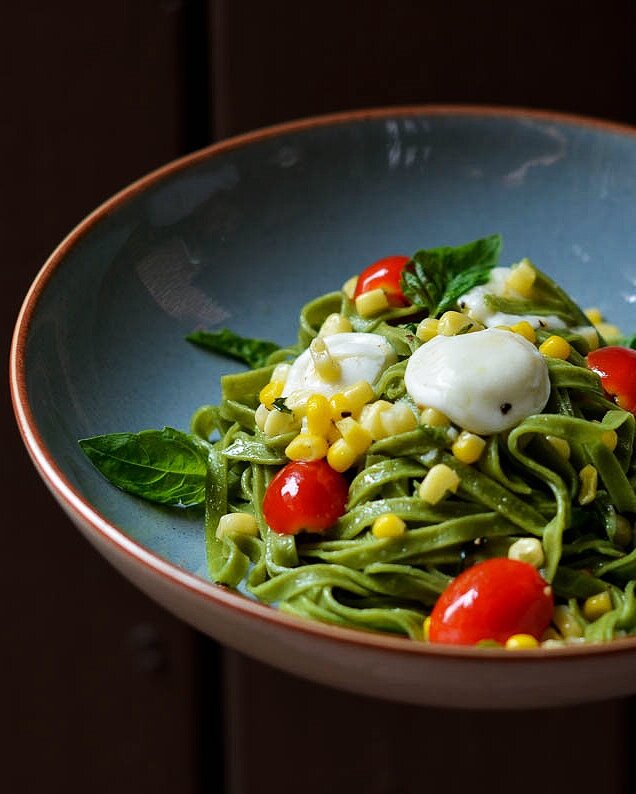A spinach pasta dish with corn and tomatoes in a blue pasta dish