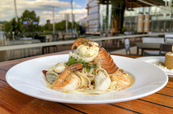 a dish of pasta with lobster and shrimp on a white plate set on a wooden table outside