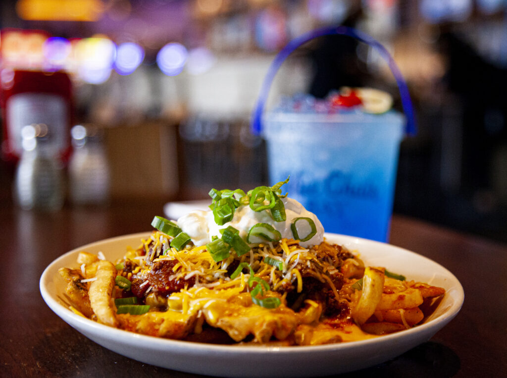 a white plate of nachos on a brown table with a blue drink in the background