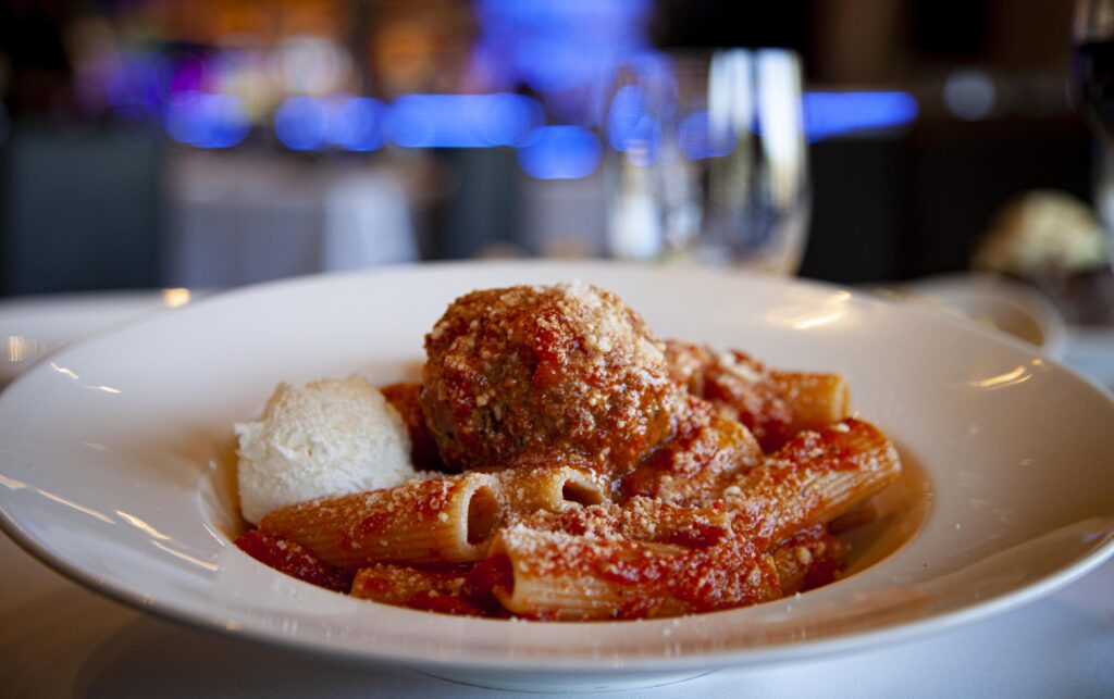 a white dish of rigatoni and meatballs on a table in a restaurant