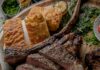 Tomahawk Steak Grilling Tips a medium rare tomahawk steak cut into several pieces and placed on a board with corn bread, grilled green onions and grilled lemons