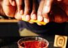 Unsung Heroes, A Juneteenth Cocktail Unsung Heroes cocktail in a rocks glass, brown in color. A hand is positioned over the top, squeezing lemon into the drink.