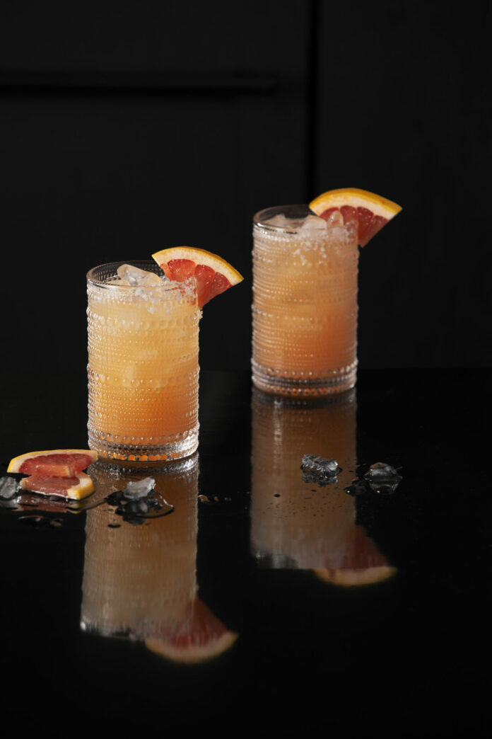 Two light orange greyhound cocktails sit in clear glasses garnished with grapefruit wedges. greyhound cocktail recipe