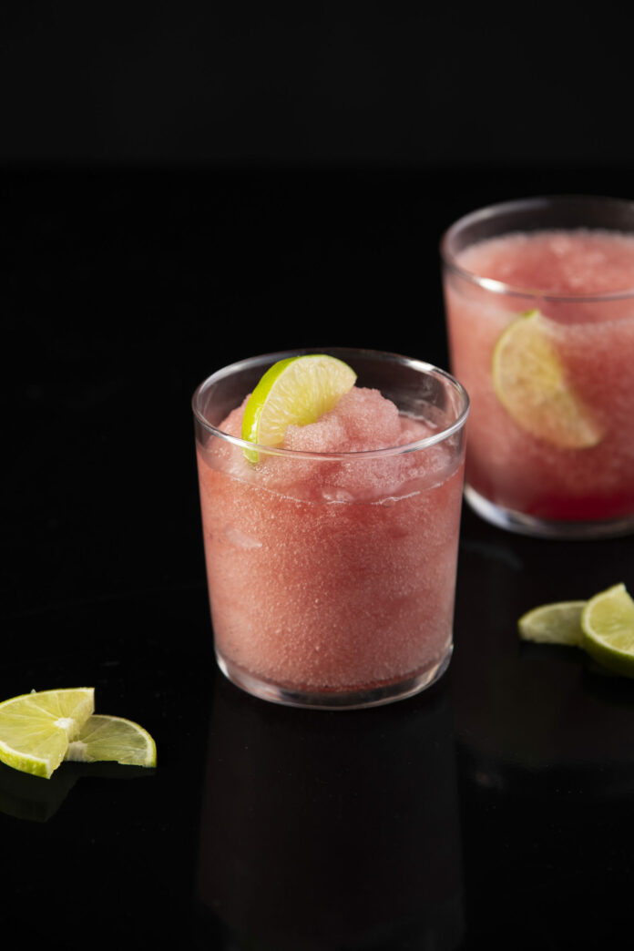 Two Frozen Cosmos, light pink in color, sit in glasses garnished by limes.