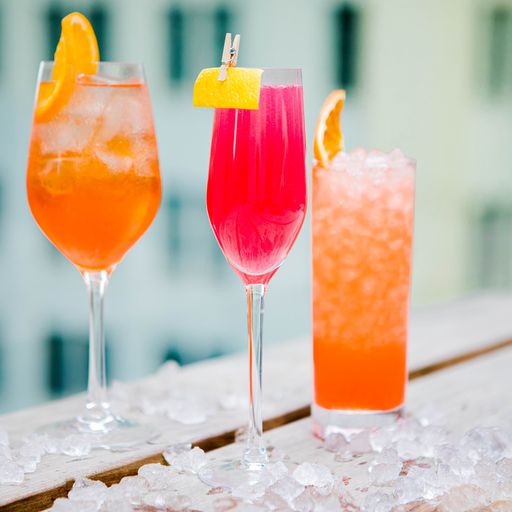 3 cocktails in a gradient of orange and pink sitting on the ledge of a rooftop bar