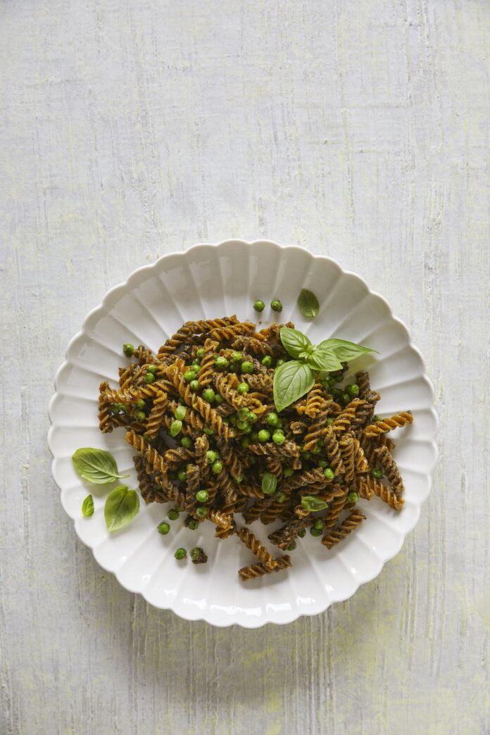 Green Pea Pasta with Sunflower Seed Pesto served in a while ceramic plate on a whitish rough surface