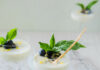 Lemon Basil Posset a 3/4 look in photo of 3 Lemon basil possets in clear coupe glasses garnished with blueberries and basil on a marble base with a white background