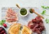 The Ultimate Grilled Cheese and Charcuterie Board for 4 a grilled cheese in the middle of a marble charcuterie board with red and purple olives and a variety of cured meats
