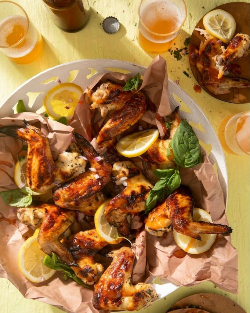 Lemon & Basil Buttermilk Grilled Chicken Wings served on a white plate with a couple of drinks