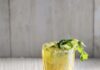 Verde Michelada a yellow and green cocktail made of verde and beer in a clear glass garnished with jalapeño and cilantro with a white background