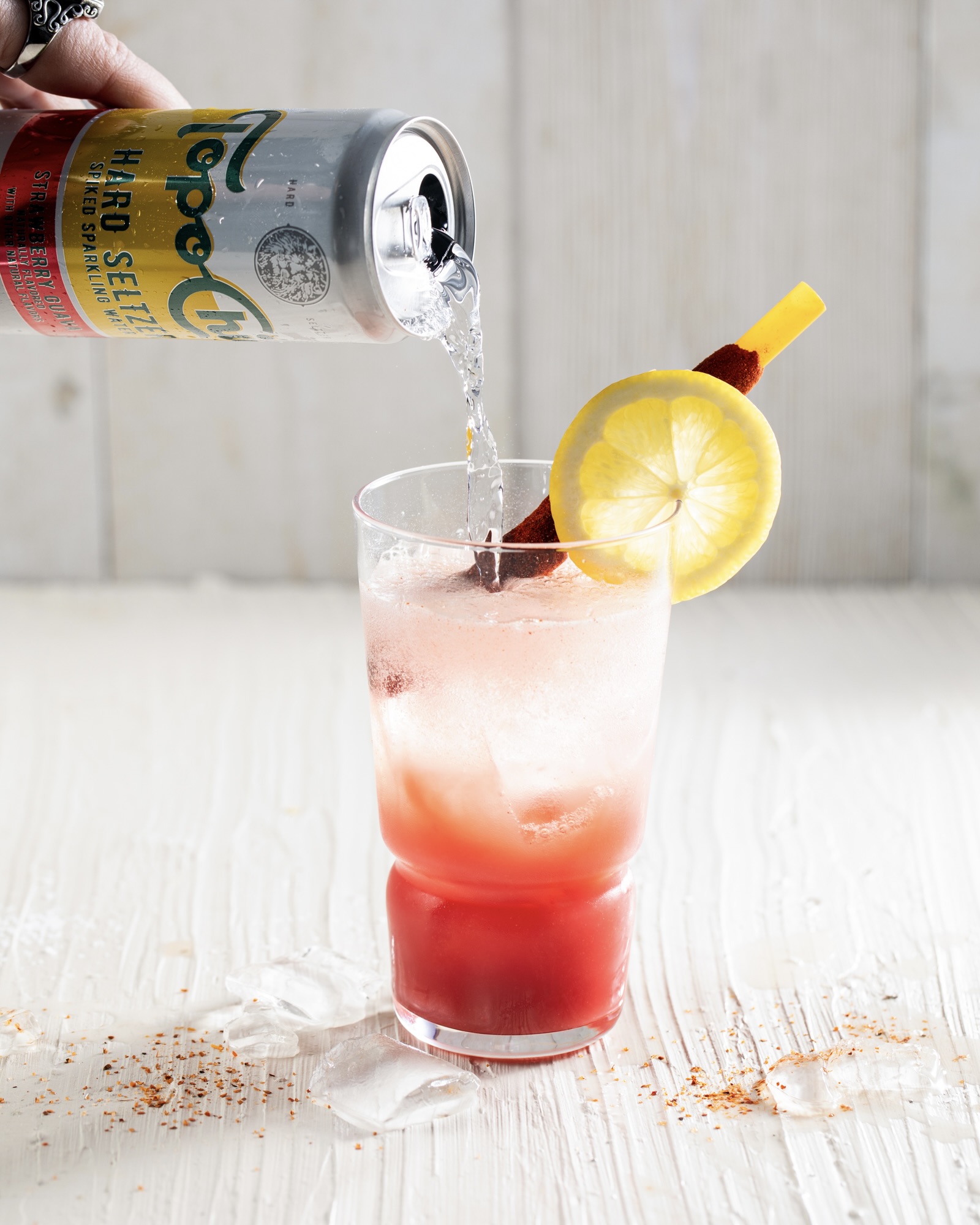 a clear glass with a white background with a pink Mexican Rosa Michelada cocktail being topped off with a can of hard seltzer. 