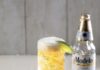 Clara Michelada a tall glass with beer and lime with a bottle of beer in the background