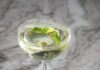 Lemon Basil Martini a lemon basil martini cocktail in a coupe glass sitting on a white and grey marble slab with fresh basil and olive oil floating on the top of the cocktail