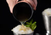 Classic Mint Julep A white hand pours a mint julep into a silver julep cup.