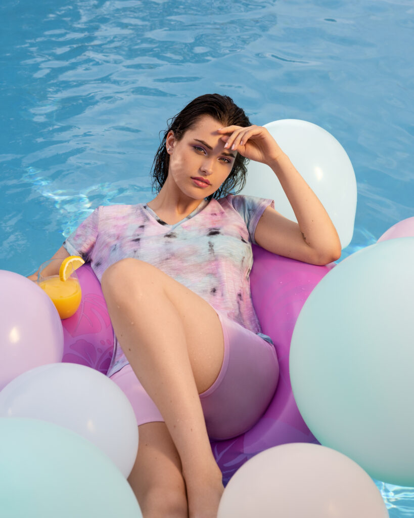 A woman in a lilac and lavender shirt floats among balloons in a pool