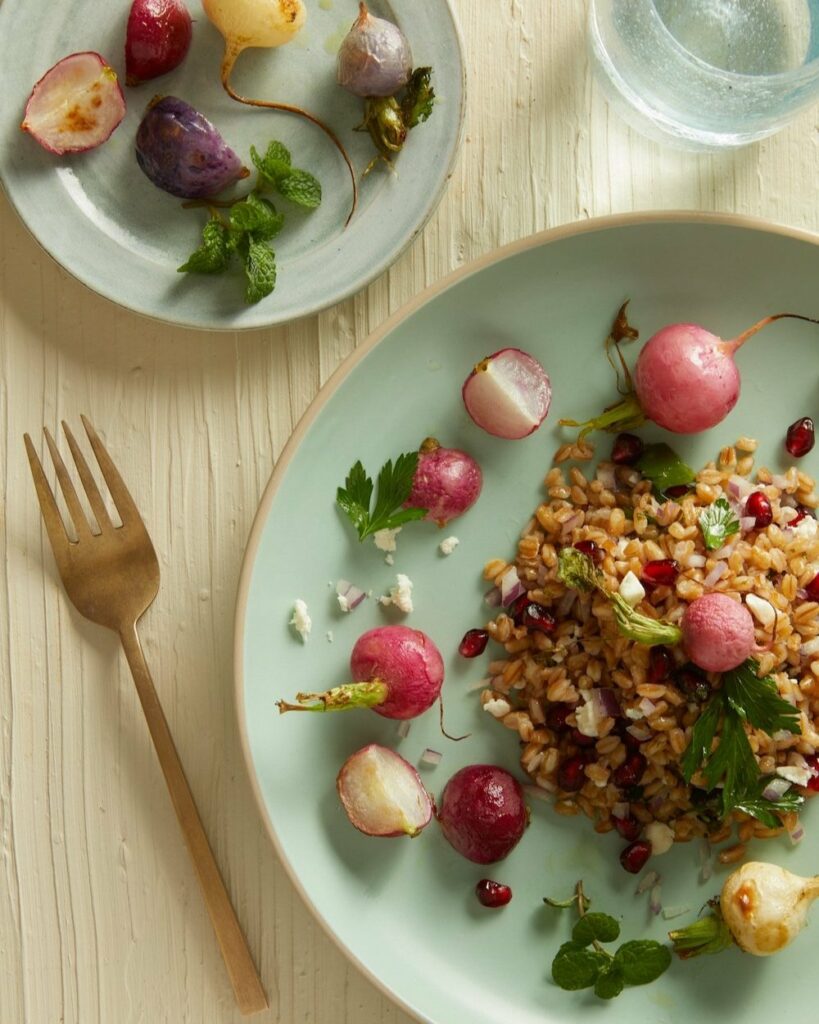 Roasted Radishes & Farro with Mint Lime Vinaigrette sits on a green plate with a gold fork positioned to the left. A farro dish
