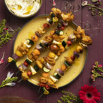 An aerial view of Shawarma Chicken Kabobs on a yellow plat surrounded by flowers. kabob recipe