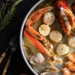 a black table with a round metal pan with clams, scallops, crab legs, lobster, and shrimp