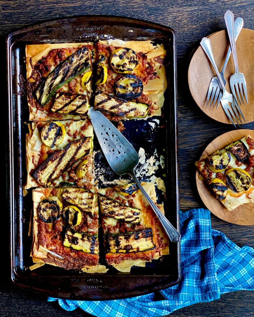 An aerial view of summer Squash Galette sitting on a baking sheet with one slice cut out. To the right are three silver forks on a plate, with the missing piece on a plate below the forks.