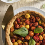 An aerial shot of a colorful tomato pie sitting on a white plate. It's garnished with basil. Tomato Pie Recipe