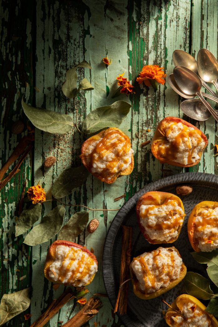 Caramel Apple Rice Pudding Flat-lay image of apples filled with caramel baked rice pudding on a weathered table. Caramel Apple Rice Pudding Recipe