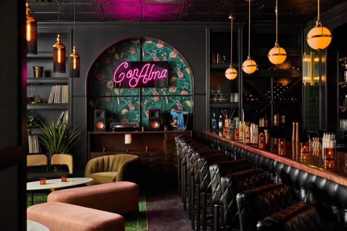 Inside of Con Alma, a neon Con Alma hangs on the wall against a colorful wallpaper